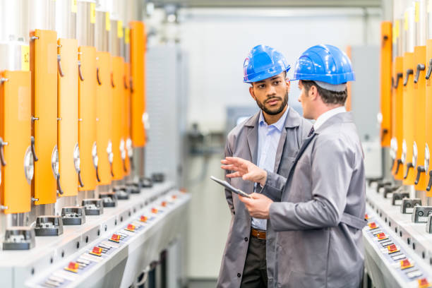 Two engineers talking while standing next to some machines in a factory.