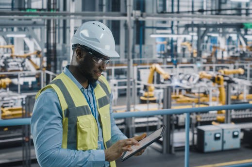 Happy African American Car Factory Engineer in High Visibility Vest Using Tablet Computer. Automotive Industrial Facility Working on Vehicle Production on Automated Technology Assembly Plant.